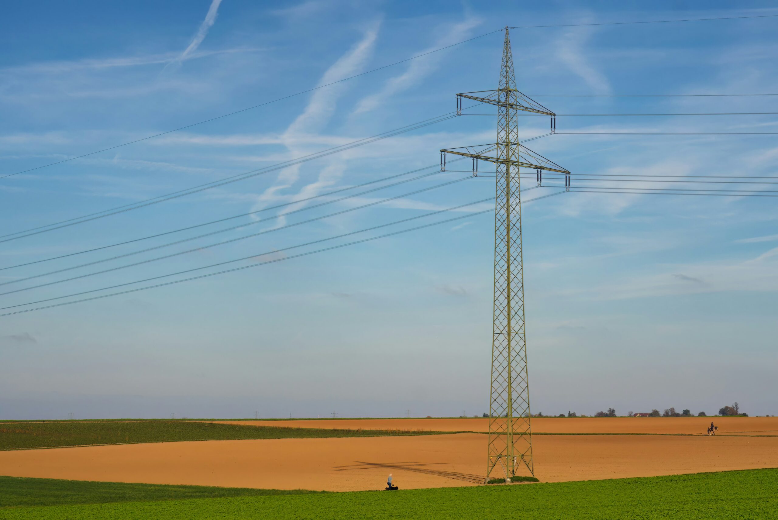 Power lines tower over a field under a bright blue sky.